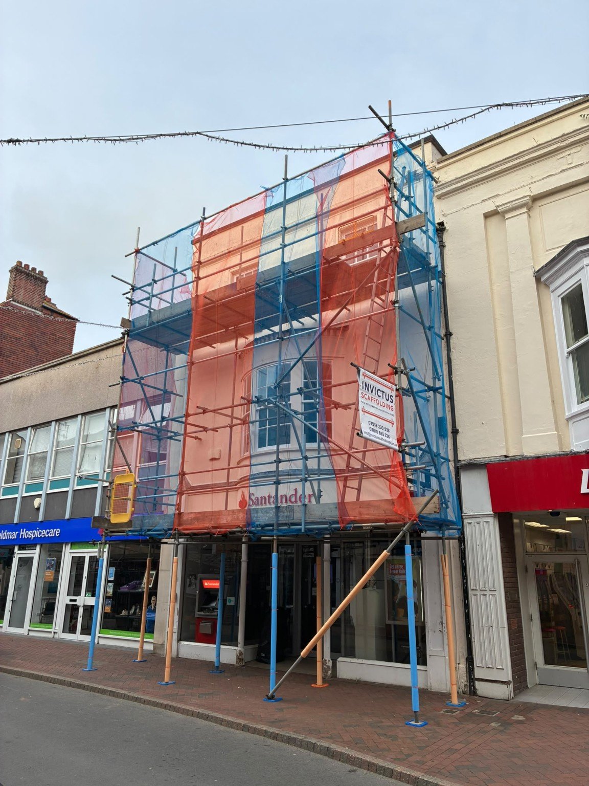 Invictus scaffold with blue and orange netting around a Santander bank frontage